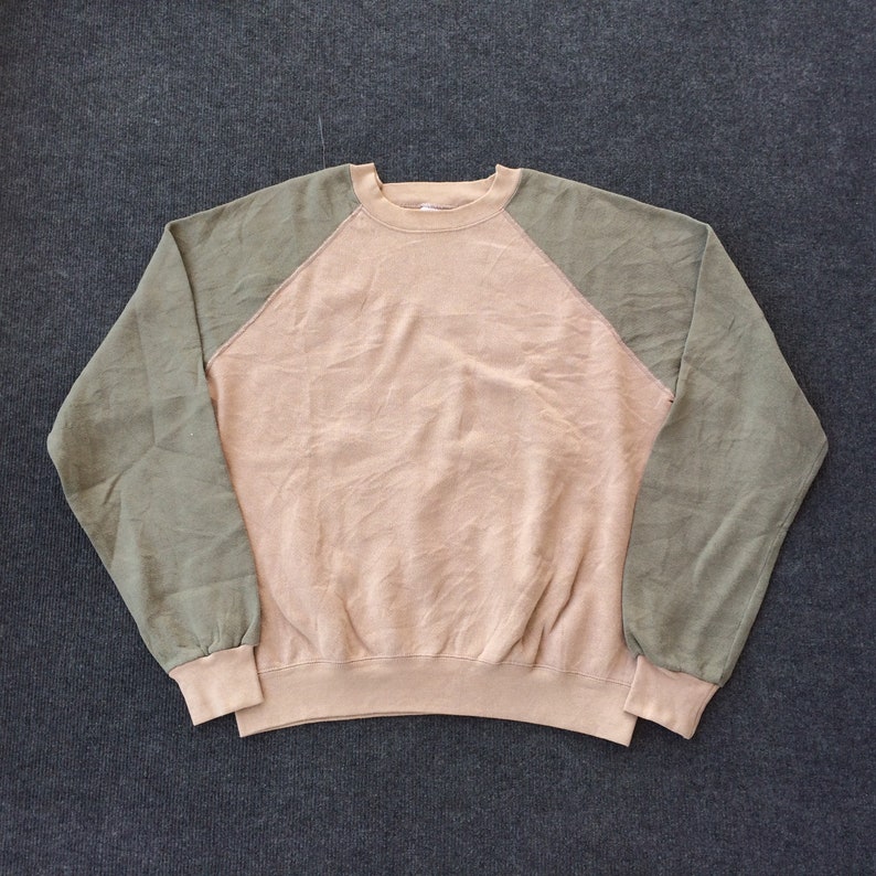 Op de afbeelding: Een beige sweatshirt met groene raglanmouwen. Het sweatshirt heeft een ronde hals en een ontspannen pasvorm.