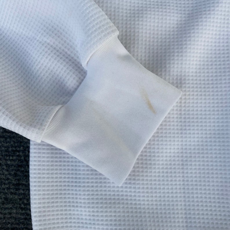 May include: White waffle knit long-sleeve shirt with a ribbed cuff. The cuff has a small, light brown stain.