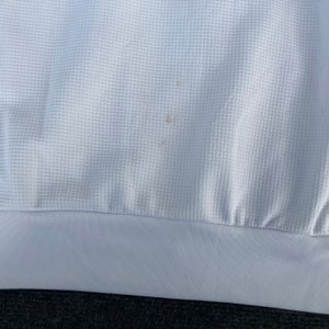 May include: White waffle knit fabric with a small brown stain. The fabric has a white hem.