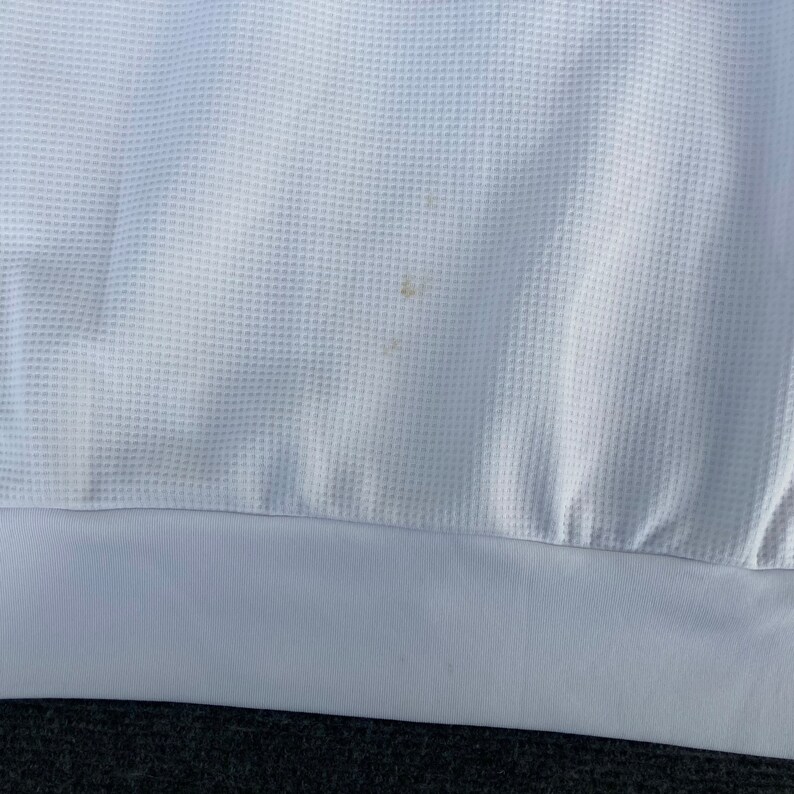 May include: White waffle knit fabric with a small brown stain. The fabric has a white hem.