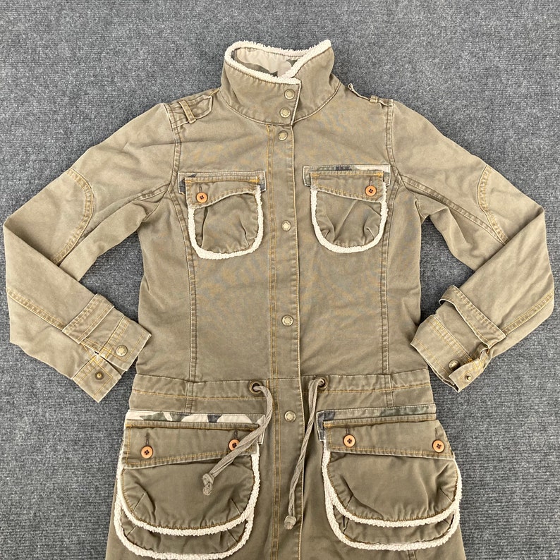 May include: A long-sleeved, brown, utility-style jacket with a sherpa lining. The jacket has multiple pockets with white trim and a drawstring waist.