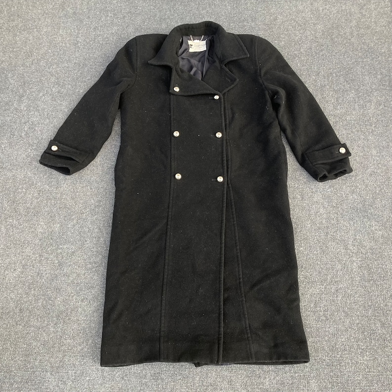 May include: A black wool coat with a double-breasted design. The coat features a notched collar, long sleeves with buttoned cuffs, and decorative silver-colored buttons. The coat is approximately 48 inches long.