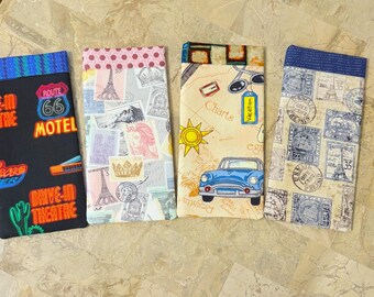 May include: Four rectangular fabric cases with travel-themed designs. One features Route 66 and Drive-In Theatre text, another has Eiffel Tower and postage stamp graphics, a third has a blue car and the word "Vacation", and the last has postage stamps.