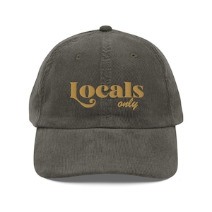 May include: A dark green corduroy baseball cap with the text "Locals only" embroidered in a light brown color.