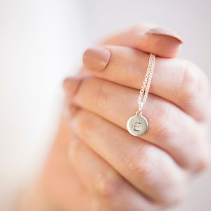 May include: A silver necklace with a round pendant featuring the letter "E" engraved on it.