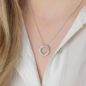 May include: A silver necklace with a four-ring pendant. The rings are intertwined and form a circle.