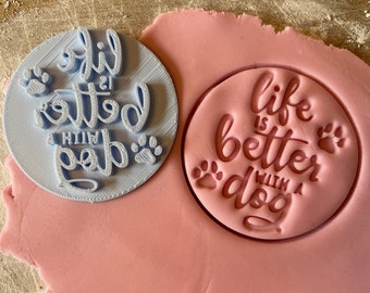 May include: Two blue and pink cookie cutters with the text "life is better with a dog" and paw prints.