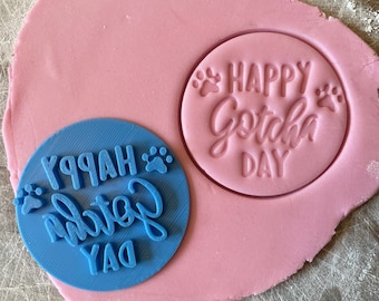 May include: Blue and pink plastic cookie cutters with the text "Happy Gotcha Day" and paw prints.