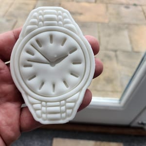 Op de afbeelding: Een gedetailleerde, witte plastic replica van een polshorloge. De wijzerplaat van het horloge heeft een klassiek ontwerp met zwarte wijzers en Romeinse cijfers.
