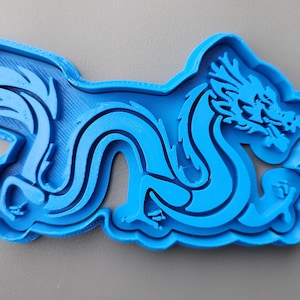 Op de afbeelding: Een felblauwe plastic draakvormige koekjesuitsteker. De uitsteker heeft een gedetailleerd ontwerp van een draak met een vloeiende staart en ingewikkelde gelaatstrekken. De draak staat in een dynamische, gebogen pose, voor het bakken.