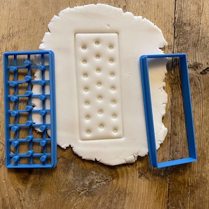 Könnte beinhalten: Drei blaue Plastik-Ausstecher auf einer Holzoberfläche. Die Ausstecher sind rechteckig und haben unterschiedliche Designs. Ein Ausstecher hat ein Gittermuster, ein anderer eine Reihe kleiner Kreise und der dritte ist ein einfacher Umriss.