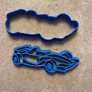 Puede incluir: Dos cortadores de galletas de pl&aacute;stico azul con forma de coche de carreras. Uno es el contorno del coche y el otro el interior detallado. Los cortadores est&aacute;n sobre una superficie texturizada de color neutro.