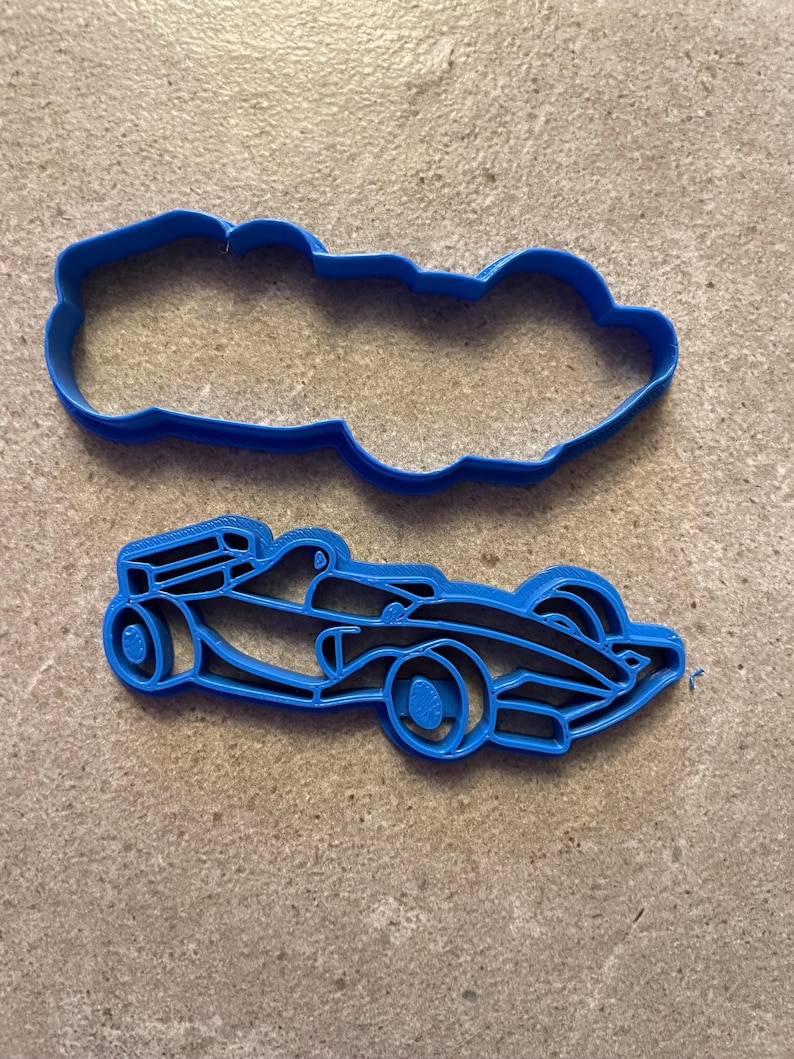 Puede incluir: Dos cortadores de galletas de pl&aacute;stico azul con forma de coche de carreras. Uno es el contorno del coche y el otro el interior detallado. Los cortadores est&aacute;n sobre una superficie texturizada de color neutro.