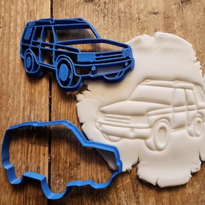 Könnte beinhalten: Blaue Plastik-Ausstecher in Form eines Autos. Die Ausstecher befinden sich auf einer Holzoberfläche mit einem weißen Fondant-Keks.