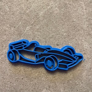 Puede incluir: Un cortador de galletas azul con forma de coche de carreras de F&oacute;rmula 1. El cortador tiene detalles como ruedas, cabina y elementos aerodin&aacute;micos. El cortador est&aacute; hecho de pl&aacute;stico.