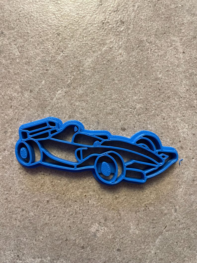 Puede incluir: Un cortador de galletas azul con forma de coche de carreras de F&oacute;rmula 1. El cortador tiene detalles como ruedas, cabina y elementos aerodin&aacute;micos. El cortador est&aacute; hecho de pl&aacute;stico.