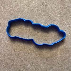 Puede incluir: Un cortador de galletas de pl&aacute;stico azul brillante con forma de nube. El cortador es de una sola pieza con un borde liso y redondeado. Est&aacute; sobre una superficie gris texturizada.
