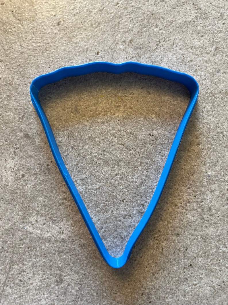 May include: A blue plastic cookie cutter shaped like a slice of pizza.