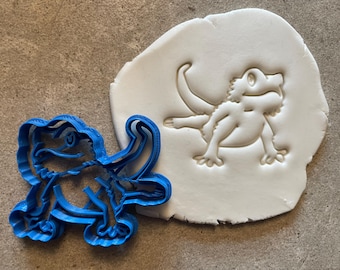 May include: A blue plastic cookie cutter shaped like a bearded dragon, with a white clay impression of the dragon next to it.