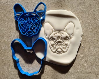 May include: A blue plastic cookie cutter in the shape of a French bulldog, next to a white fondant cookie with an embossed French bulldog design.
