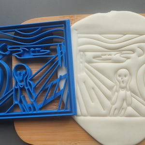 May include: A blue plastic cookie cutter depicting Edvard Munch's "The Scream" artwork, alongside a sugar cookie with the design imprinted. The cookie rests on a wooden board.