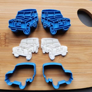 May include: A wooden cutting board displays six blue and white car-shaped cookie cutters. Two blue cutters are outlines, two are solid blue, and two are white. The cutters are arranged in three pairs.