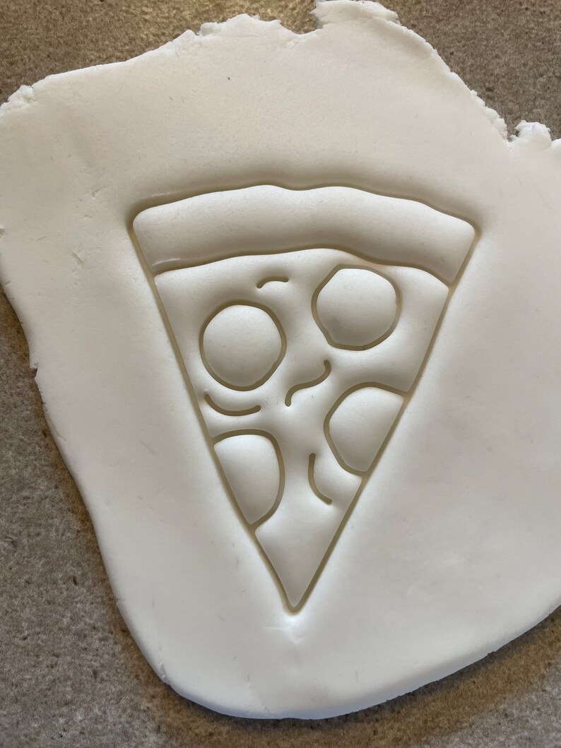 May include: A white clay surface with an embossed image of a pizza slice. The pizza slice has a crust, cheese, and pepperoni.