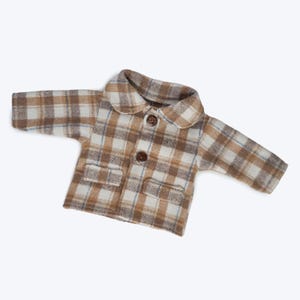 Puede incluir: Una chaqueta de bebé de cuadros marrones y blancos con cuello blanco y dos botones marrones.