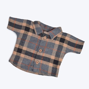 Puede incluir: Una camisa de manga corta a cuadros con un frente abotonado con cuello. La camisa es una mezcla de cuadros marrones, grises y negros.