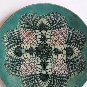 Könnte beinhalten: Ein tealfarbener Keramikteller mit einem schwarzen und weißen Spitzenmuster in der Mitte.