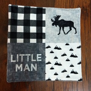 May include: A black and white checkered fabric square with a gray fabric square with the text "LITTLE MAN" printed in white. The other two squares are gray with a black moose silhouette and a white fabric with a black mountain pattern.