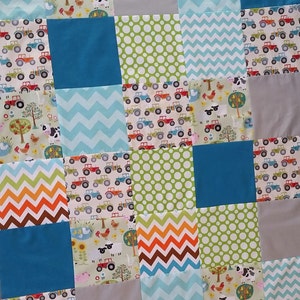 May include: A patchwork quilt with a variety of colorful fabrics. The quilt features a blue, green, and white chevron pattern, a green polka dot pattern, and a pattern of red tractors on a white background.
