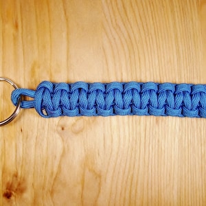 May include: A blue paracord keychain with a silver key ring. The keychain is made with a braided paracord.