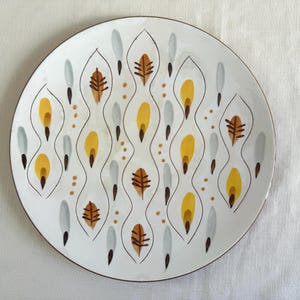 May include: A white ceramic mug with a black handle and the text "But First, Coffee" in a bold, black font. The mug is set against a blurred background, suggesting a cozy setting.