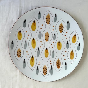 May include: White ceramic plate with a brown rim, featuring a repeating pattern of yellow, gray, and brown teardrop and leaf shapes. The design includes small brown dots and black accents, creating a mid-century modern aesthetic.