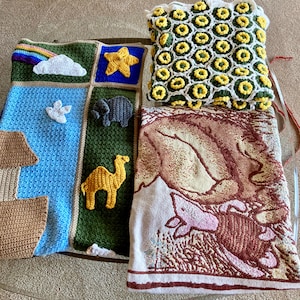 May include: A collection of handmade blankets and pillows. One blanket features a rainbow, cloud, star, and animal appliqués. Another has a repeating yellow and green pattern. A third blanket has a brown and pink illustration.