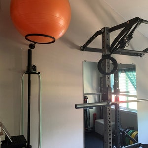 May include: A home gym setup with a black weight rack, a pull-up bar, and a large orange exercise ball hanging from the wall.