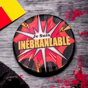 May include: A black and red button with a white starburst and the text "Je Suis INÉBRANABLE" in white.