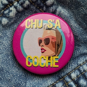 May include: A round, pink button with the text "CHU S'A COCHE" in yellow. The button features an illustration of a woman wearing sunglasses. The background is a denim texture.