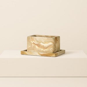 Peut inclure: Un pot rectangulaire avec une soucoupe rectangulaire assortie. Le pot et la soucoupe présentent un motif marbré beige et marron. Le pot est posé sur une surface blanche.
