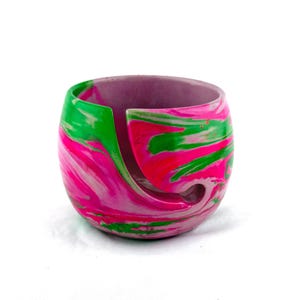 Handmade yarn bowl with bright pink, green, and white marbled swirl design, crafted for knitters and crocheters who want both function and style. This smooth, glossy yarn holder features a curved yarn guide slot to keep yarn feeding cleanly without tangles. A colorful knitting bowl perfect for crochet projects, fiber arts, craft rooms, or gifting to knitters, crocheters, and yarn lovers who appreciate unique handmade tools.