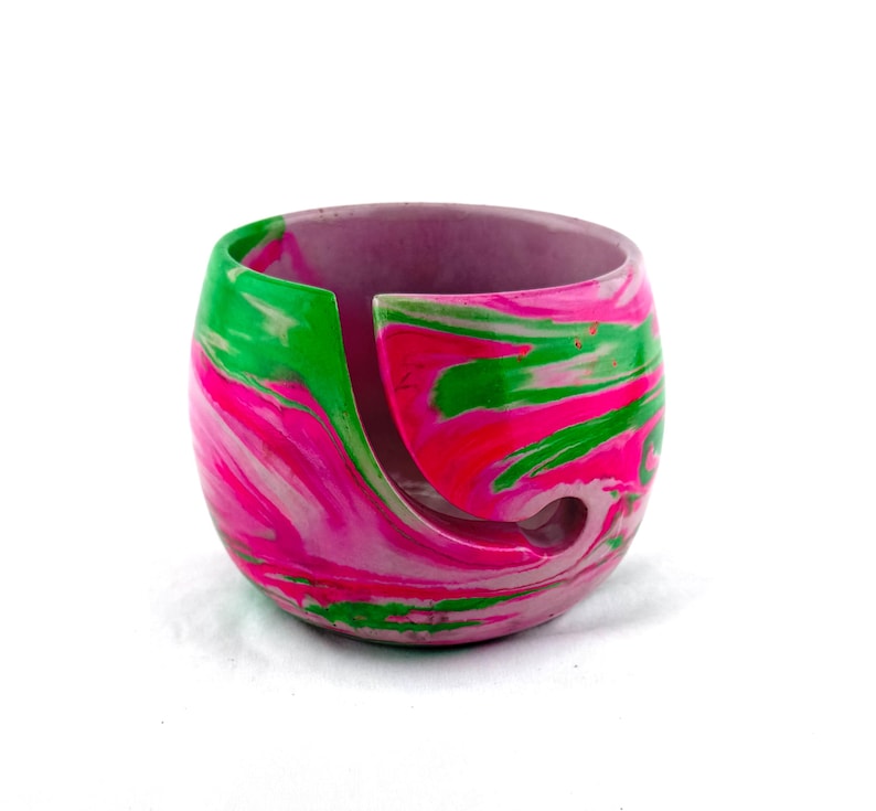 Handmade yarn bowl with bright pink, green, and white marbled swirl design, crafted for knitters and crocheters who want both function and style. This smooth, glossy yarn holder features a curved yarn guide slot to keep yarn feeding cleanly without tangles. A colorful knitting bowl perfect for crochet projects, fiber arts, craft rooms, or gifting to knitters, crocheters, and yarn lovers who appreciate unique handmade tools.