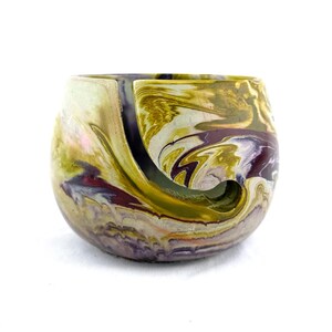 Handmade marbled cement yarn bowl in earthy mustard, plum, and cream tones with a smooth spiral cutout to guide the strand. Modern concrete yarn holder for knitters and crocheters keeps yarn cakes and balls from tangling or rolling, a durable artisan knitting accessory and unique gift for fiber artists who love colorful, contemporary craft room decor.