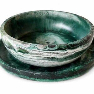May include: A round bowl and matching saucer set featuring a marbled pattern in shades of deep forest green, emerald, and white. The bowl has a smooth, curved interior with a small circular drain hole at the base, while the saucer is flat.