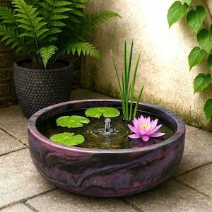 Könnte beinhalten: Dekorativer Wassergarten im Freien mit lila Marmor-Finish. Der Brunnen hat einen kleinen Wasserstrahl, Seerosenblätter und eine rosa Seerose. Ein Topffarn und Kletterpflanzen befinden sich im Hintergrund.