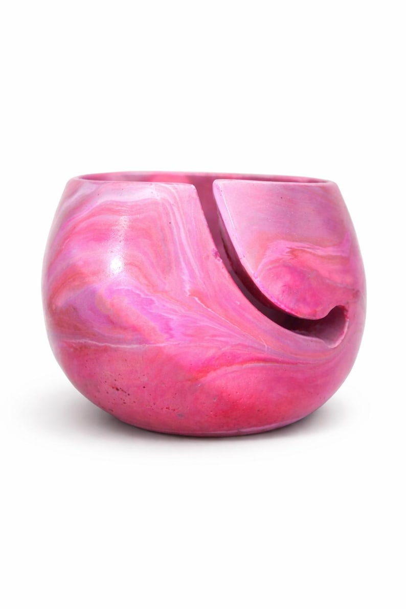 Handmade marbled yarn bowl in pink, coral, and soft white tones with a smooth glossy finish and curved yarn guide slot. This ceramic look yarn holder keeps yarn clean, untangled, and rolling smoothly while knitting or crocheting. Perfect for knitters, crocheters, fiber artists, cozy craft room decor. Unique swirl pattern makes each bowl one of a kind. Great gift for knitters, crochet gift for mom gift for crafters and handcrafted pottery collections.