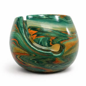 Handmade ceramic yarn bowl with rich green, copper, and earthy swirl marbling inspired by natural stone and ocean patina. This glossy yarn holder features a smooth spiral guide slot to keep yarn feeding cleanly while knitting or crocheting. Perfect for knitters, crocheters, fiber artists, and cozy craft room decor. Unique marbled pattern makes every bowl one of a kind. Beautiful gift for knitters, crochet lovers, yarn collectors, and handmade pottery fans.