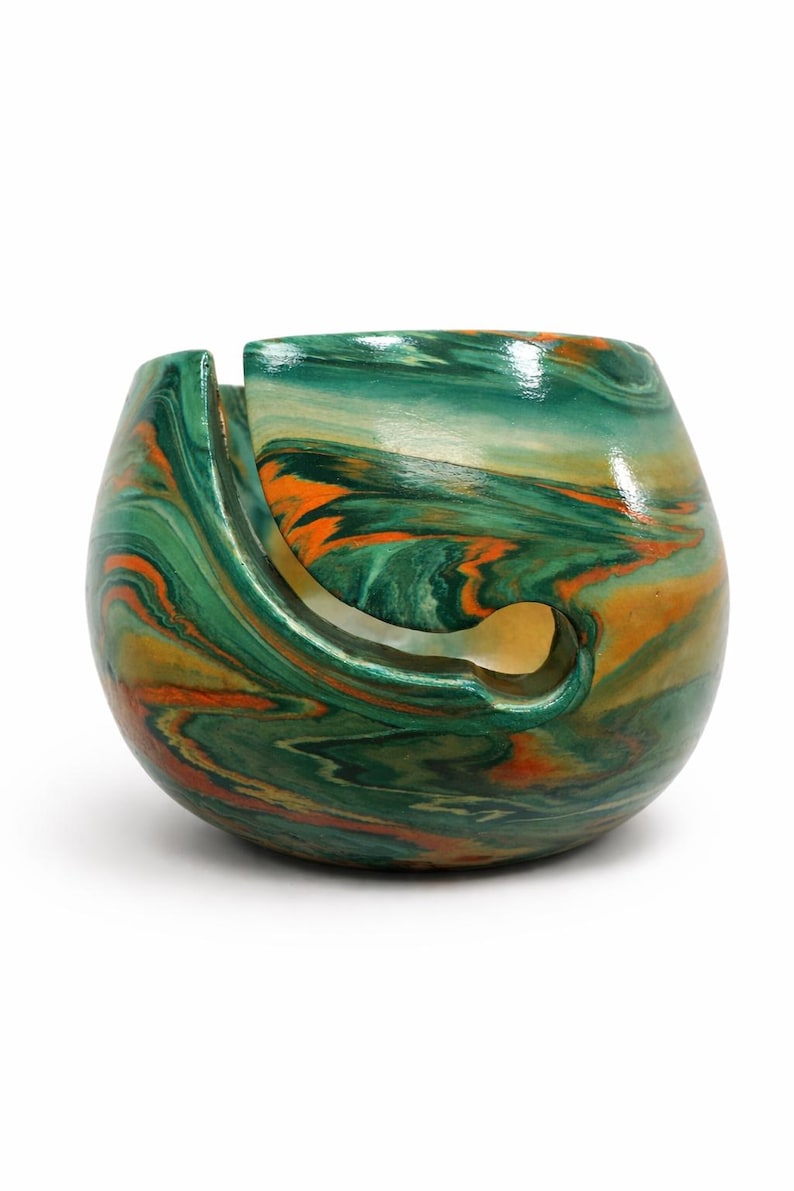Handmade ceramic yarn bowl with rich green, copper, and earthy swirl marbling inspired by natural stone and ocean patina. This glossy yarn holder features a smooth spiral guide slot to keep yarn feeding cleanly while knitting or crocheting. Perfect for knitters, crocheters, fiber artists, and cozy craft room decor. Unique marbled pattern makes every bowl one of a kind. Beautiful gift for knitters, crochet lovers, yarn collectors, and handmade pottery fans.