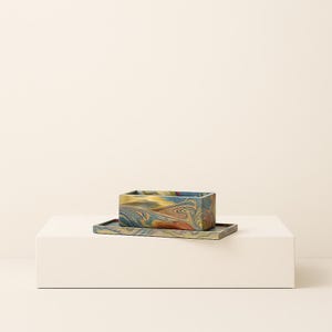 Könnte beinhalten: Ein rechteckiger Pflanztopf und eine passende Schale mit einem Wirbelmuster in Blau-, Gelb- und Rottönen. Der Pflanztopf steht auf einer weißen Oberfläche vor einem neutralen Hintergrund. Der Pflanztopf ist etwa 15 cm lang.