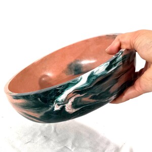 May include: A shallow, oval-shaped bowl featuring a marbled pattern of deep forest green, white, and soft peach tones. The interior of the bowl has a smooth, solid peach-colored finish, while the exterior displays a swirling, multi-colored design.